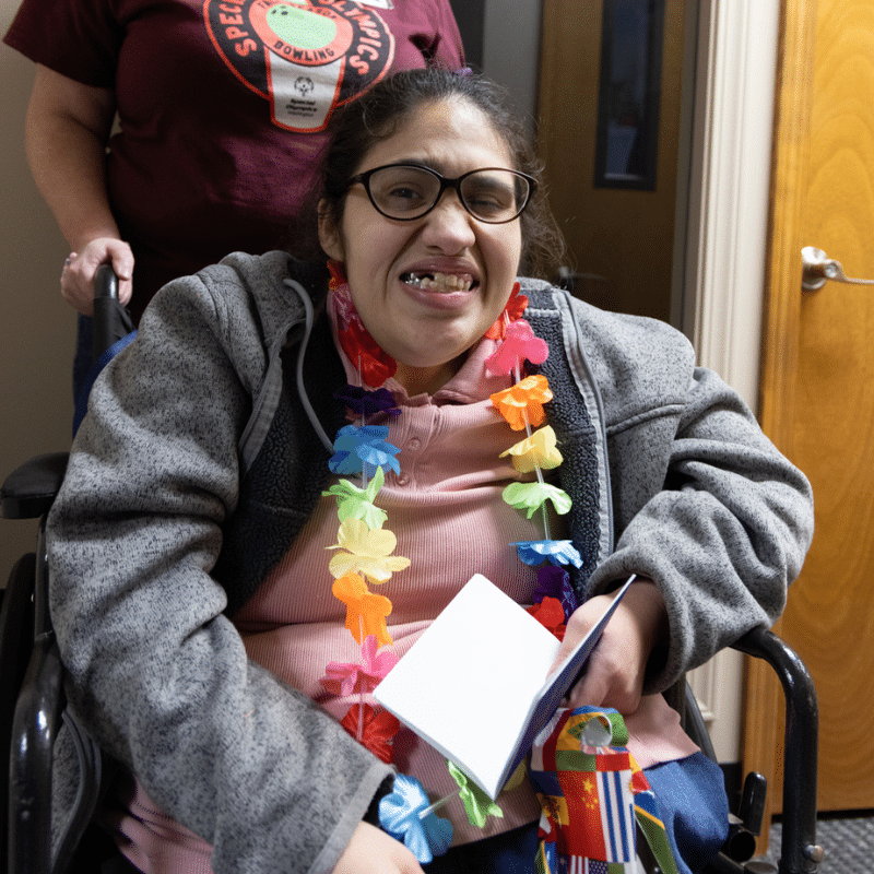 A Community Center client in a wheelchair smiling at the camera while wearing a lei flower necklace.